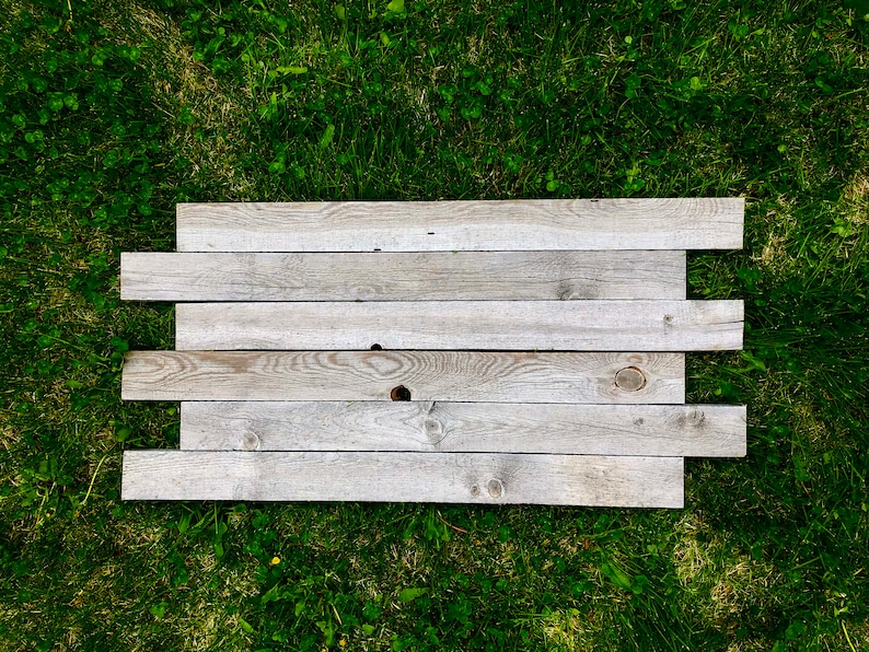 May include: A weathered wooden sign made of six horizontal planks, laid out on a bed of green grass.