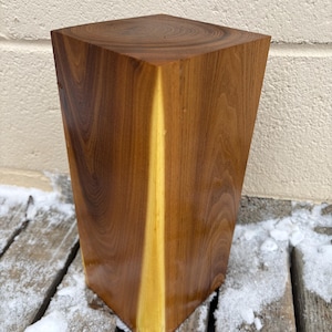 May include: A solid wood block with a natural wood finish. The block has a light brown color with a yellow stripe running down the center. The block is sitting on a wooden surface.