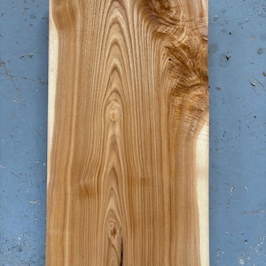 May include: A close-up of a piece of wood with a natural wood grain pattern. The wood is light brown in color and has a smooth surface.