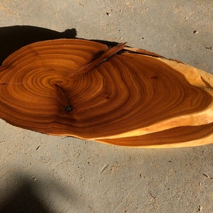 May include: A large, round wooden slab with a beautiful grain pattern. The slab is a natural wood color with darker brown rings. The slab is thick and has a smooth surface.
