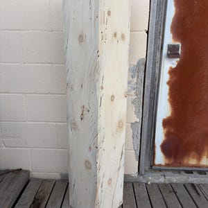 May include: A large, rectangular block of wood with a natural, light brown color and a knotty grain pattern. The wood is rough-hewn and has a rustic appearance.