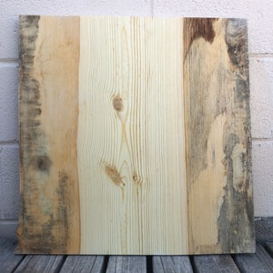 May include: A rectangular piece of reclaimed wood with a natural wood grain pattern. The wood has a light brown color with darker brown streaks and knots. The wood is smooth and has a slightly weathered look.