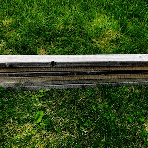 May include: A stack of weathered wooden boards, likely reclaimed wood, lying on a bed of green grass.