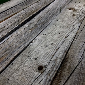 May include: Close-up of weathered wooden planks, showing the natural grain and texture of the wood. The planks are arranged in a diagonal pattern, creating a rustic and aged look.
