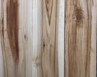 May include: Three wooden planks with a natural wood grain pattern. The planks have a light brown color with darker brown streaks and knots.