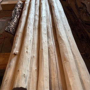 May include: Close-up of six unfinished, light brown wooden logs, stacked and aligned, with a rough, textured surface. The logs are all the same length and diameter, and they are arranged in a neat row.