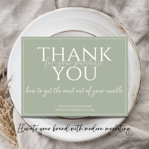 May include: A green thank you card with white text that says "THANK for your purchase YOU how to get the most out of your candle YOUR BUSINESS NAME WWW.YOURWEBSITE.COM". The card is on a white plate with a beige fabric background.