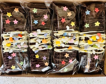 May include: Four individually wrapped chocolate bars with white chocolate drizzle and colorful sprinkles. The bars are arranged in a box and are ready to be enjoyed.