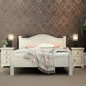 Puede incluir: Estructura de cama de madera blanca con un cabecero que tiene una parte superior curva. La cama está hecha con una funda nórdica blanca y una manta de cuadros. Dos mesitas de noche con cajones están a cada lado de la cama, cada una con una pequeña lámpara.