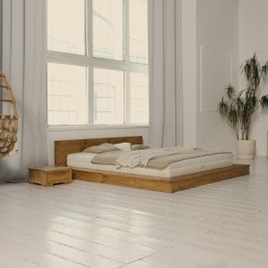 Könnte beinhalten: Ein hölzerner Plattform-Bettgestell mit einer hellbraunen Oberfläche. Das Bett hat eine weiße Matratze und eine beige Decke. Neben dem Bett steht ein kleiner Nachttisch aus Holz.