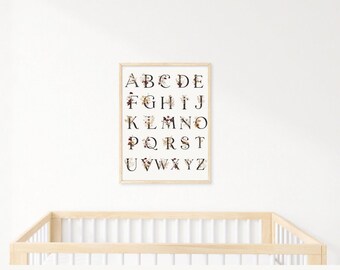 Può includere: Una stampa alfabetica incorniciata con accenti floreali in tonalità bordeaux e beige. Le lettere sono in un carattere serif nero. La stampa è appesa a un muro bianco sopra una culla di legno.