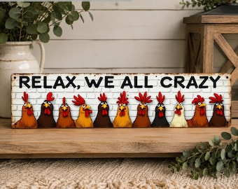 May include: A rectangular metal sign featuring a white brick wall background and the black text RELAX, WE ALL CRAZY. Below the text, a row of eleven cartoon chickens in various shades of brown, black, and white are lined up with red combs.
