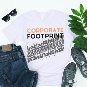Può includere: Maglietta bianca con il testo "CORPORATE FOOTPRINT" in nero e arancione. Un grafico di battistrada del pneumatico grigio si trova sotto il testo.