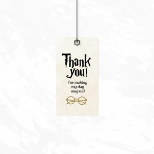May include: A white tag with black text that reads "Thank you! for making my day magical".  The tag has a gold pair of glasses printed on it.