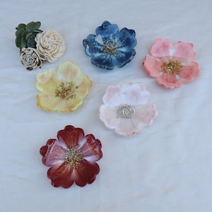 Op de afbeelding: Vijf harsbloemvormige schalen in verschillende kleuren, waaronder blauw, roze, geel, wit en rood. Elke schaal heeft een gouden glitteraccent en is perfect voor het bewaren van kleine items zoals ringen of oorbellen.