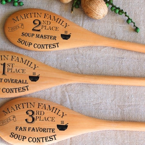 May include: Three wooden spoons with black engraved text. The spoons are labeled "Martin Family" and show the years 2021, 2022, and 2023. The spoons are labeled "1st Place", "2nd Place", and "3rd Place" and have the text "Soup Contest" on each.
