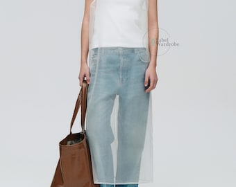 Puede incluir: Un vestido maxi blanco transparente con un top blanco debajo. El vestido se lleva con jeans azules y un bolso tote de cuero marrón.