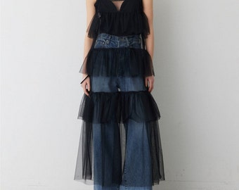 Puede incluir: Una falda de tul negro con múltiples capas de volantes. La falda se lleva sobre un par de pantalones vaqueros azules.