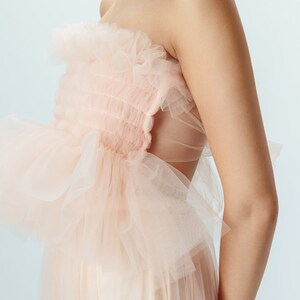 May include: A strapless dress made of delicate pink tulle with a ruffled bodice and a flowing skirt.