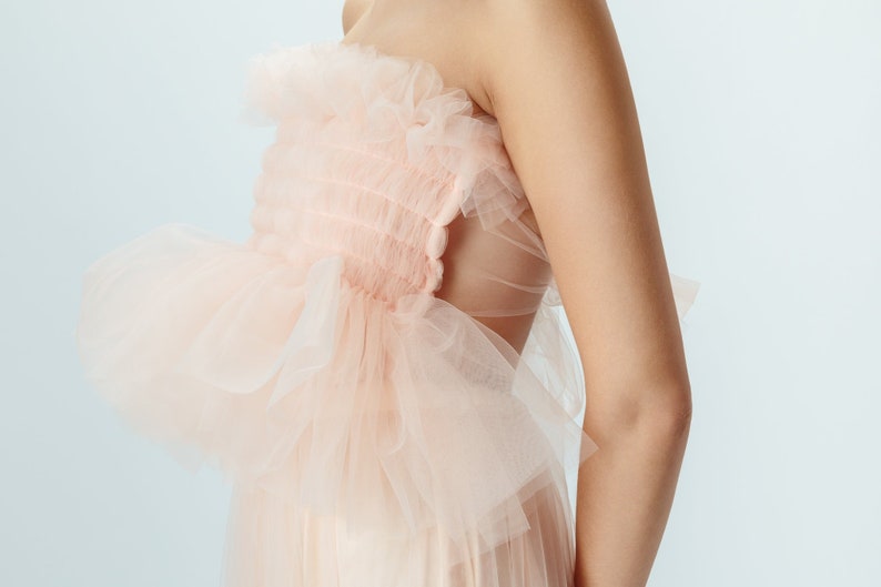 May include: A strapless dress made of delicate pink tulle with a ruffled bodice and a flowing skirt.