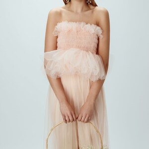 May include: A woman wearing a pink tulle dress with a ruffled bodice. She is holding a wicker basket with white flowers.