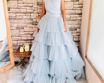 May include: A light blue formal gown with a layered tulle skirt and a fitted bodice. The bodice has a sheer neckline and cap sleeves. The gown's skirt cascades to the floor, creating a dramatic effect. The dress is suitable for special occasions.