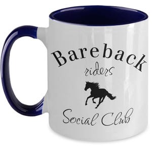 May include: White ceramic coffee mug with a blue rim and handle. The mug has a black silhouette of a horse running and the text "Bareback riders Social Club".