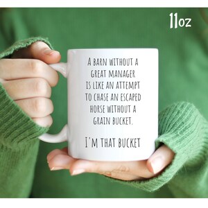 May include: White ceramic mug with black text that reads "A barn without a great manager is like an attempt to chase an escaped horse without a grain bucket. I'm that bucket." The mug is 11 ounces.