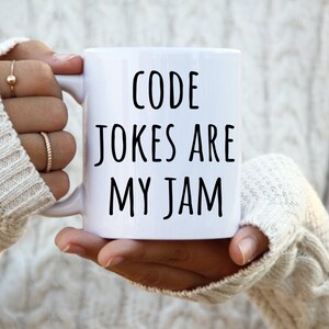 May include: White ceramic mug with black text that reads "CODE JOKES ARE MY JAM".