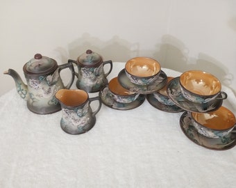 May include: A vintage Japanese tea set with a dragon design. The set includes a teapot, creamer, and four teacups and saucers. The teacups and saucers are decorated with a floral pattern.