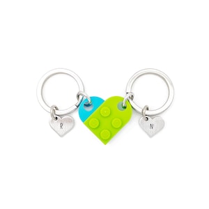 Puede incluir: Dos llaveros plateados con dijes en forma de coraz&oacute;n. Los dijes est&aacute;n conectados por un dije en forma de coraz&oacute;n verde y azul con un dise&ntilde;o tipo Lego. Los dijes est&aacute;n grabados con las letras "R" y "N".