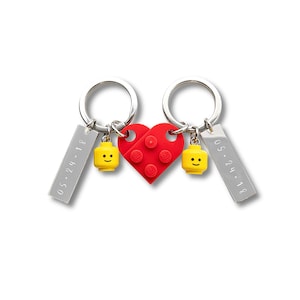 May include: Two keychains with silver rings, each featuring a yellow Lego figure with a smiling face. A red Lego heart is in the center. Each keychain has a rectangular tag with the date "05.24.18" engraved.