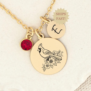 May include: Gold necklace with a cardinal bird charm, a red crystal charm, and a charm with the letter "L" engraved on it.