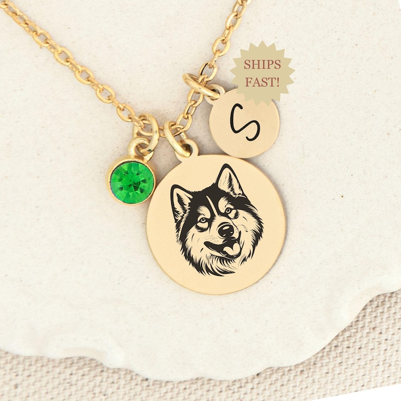 May include: Gold necklace with a green gemstone, a round charm with a husky dog silhouette, and a charm with the letter "S".