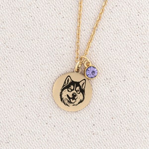 May include: Gold necklace with a round pendant featuring a black and white husky dog silhouette. The pendant has a small purple crystal charm attached.