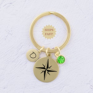 May include: Gold compass keychain with a green crystal charm and a letter D charm. The keychain has a gold ring and a tag that says "Ships Fast!"