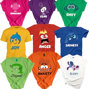 May include: A collection of nine colorful t-shirts, each featuring a different character and emotion from the animated movie "Inside Out." The shirts are in various colors, including pink, purple, green, yellow, red, blue, orange, and white, with the emotion's name printed below the character.
