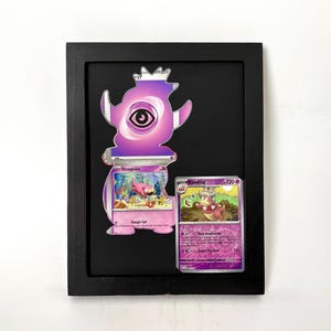 May include: Framed artwork featuring a purple Slowpoke-themed design and two Pokémon trading cards. The cards are displayed on a black background within a black frame. The artwork is a unique piece for Pokémon fans.