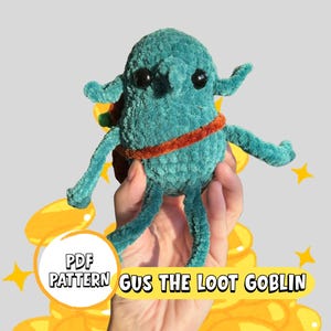 Op de afbeelding: Een turquoise pluche goblin met zwarte ogen, kleine oren en uitgestrekte armen. Hij heeft een oranje riem en een kleine rugzak. De tekst "PDF PATTERN GUS THE LOOT GOBLIN" staat op de afbeelding. Gouden munten en sterren staan op de achtergrond.