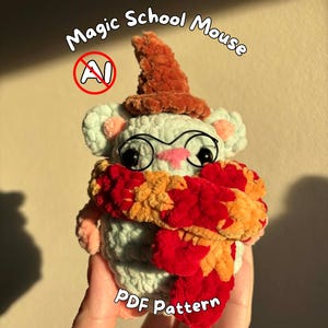May include: A light blue crocheted mouse plush toy wearing a brown pointed hat, black wire-rimmed glasses, and a thick, textured scarf with alternating orange and red sections. The text Magic School Mouse and PDF Pattern appear on the image.
