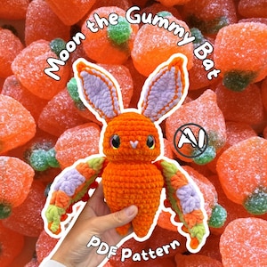 May include: A crochet bat toy named Moon the Gummy Bat with an orange body, lavender inner ears, and multicoloured wings in orange, lavender, and light green. The text Moon the Gummy Bat and PDF Pattern is visible on the image.