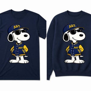 Op de afbeelding: Twee marineblauwe tops. De ene is een t-shirt, de andere een sweatshirt. Beide hebben een cartoonhond met een zonnebril, een baseballpet en een varsity-jack. De jas en pet van de hond tonen de letters "A&T".
