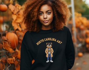 May include: Black sweatshirt featuring a cartoon bear wearing sunglasses and a coat. The text "NORTH CAROLINA A&T" is printed in gold above the bear.