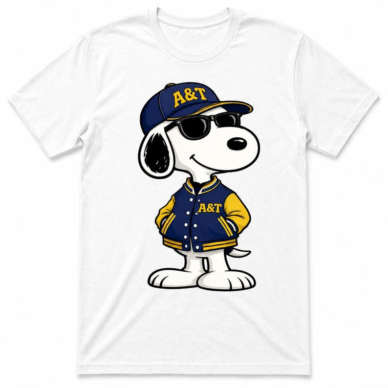 Op de afbeelding: Wit T-shirt met een cartoonhond die een marineblauwe baseballcap en jas met gele accenten draagt. Op de pet en jas staan de letters "A&T". De hond draagt ook een zwarte zonnebril.