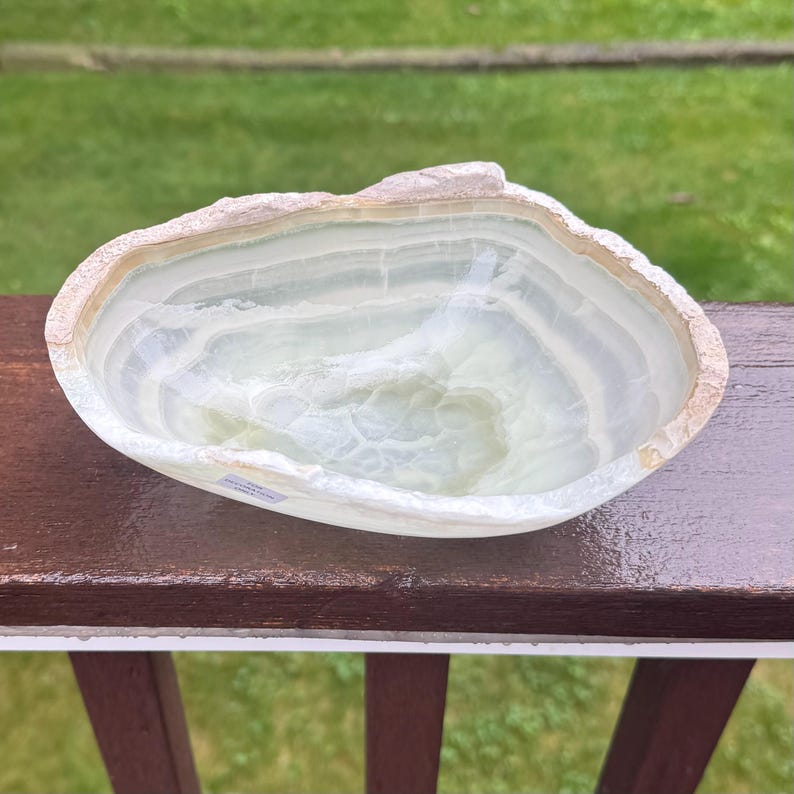 May include: A natural stone bowl with a light green and white color scheme. The bowl has a unique, organic shape with a rough, textured edge. The interior has a smooth, polished surface.