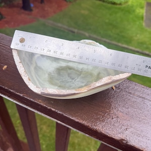 May include: A translucent, light green onyx bowl with a rough, natural edge. The bowl is approximately 6 inches in diameter and is set on a wooden surface. The bowl's interior has a marbled appearance.