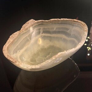 May include: A natural stone bowl with a light green and white layered pattern. The bowl has a rough, textured edge and a smooth, polished interior. The bowl is likely used for decorative purposes.