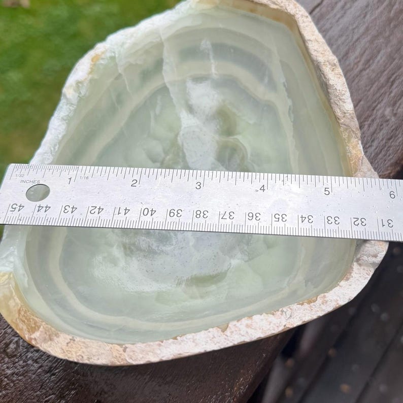 May include: A light green onyx bowl with a natural, rough edge. The bowl is approximately 6 inches wide. The interior has a smooth, polished surface with visible layers of color. A ruler is placed across the bowl for measurement.