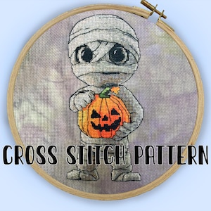 Könnte beinhalten: Kreuzstichmuster mit einer Mumie, die einen orangefarbenen Kürbis hält. Die Mumie ist in Bandagen gewickelt und hat große schwarze Augen. Der Text "CROSS STITCH PATTERN" wird in schwarzen Buchstaben angezeigt.