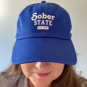 Peut inclure: Une casquette de baseball bleu roi avec un texte brodé blanc qui dit "Sober State EST. 2017".